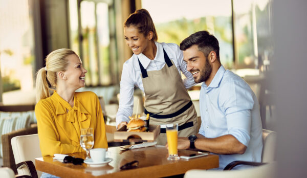 Happy couple enjoying in a restaurant while the waitress is serving them food. Focus is on waitress. Copy space.